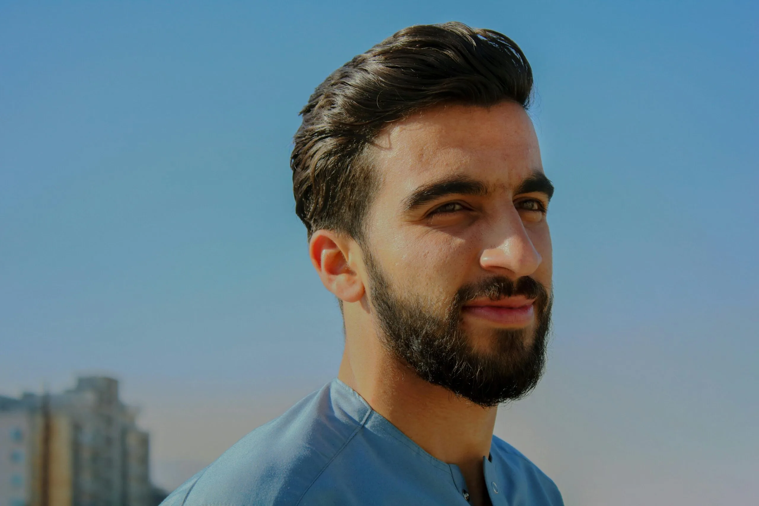 pexels-photo-819530-819530-2 A close-up outdoor portrait of a young man with facial hair, exuding confidence under a clear sky.